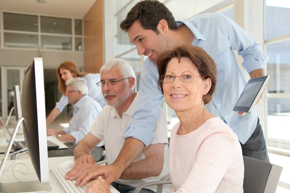 Mehrere Personen sitzen lächelnd an ihren Computern und arbeiten gemeinsam in einem hellen Raum.